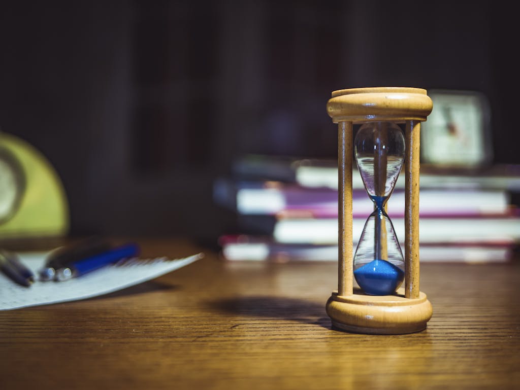 Maximizing Your Potential: Strategies for Online Learners Close-up of a wooden hourglass on a desk, alongside books and pens, suggesting focused study or time management.