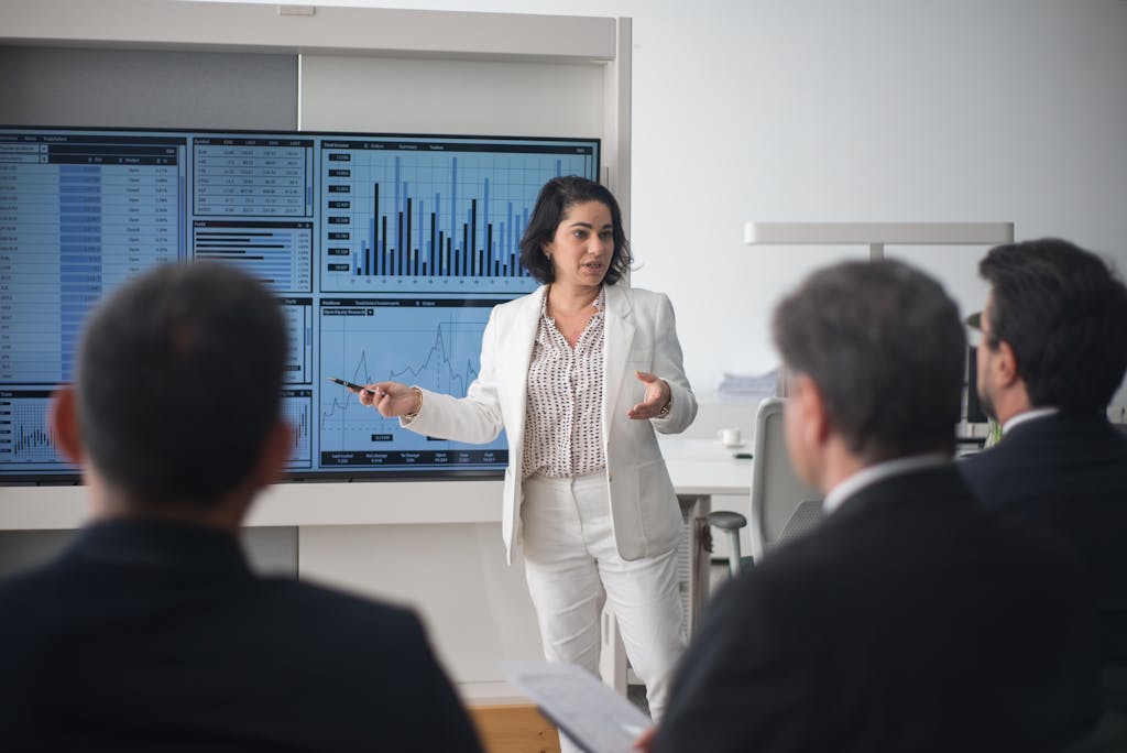 Professional woman presenting stock market data in a modern office, representing an Online MBA in Business Administration program. Hallford University.